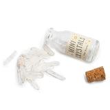 A miniature clear glass bottle labeled 'MINI CRYSTALS' with several small translucent crystal points scattered beside it and a cork stopper, photographed on a white background.