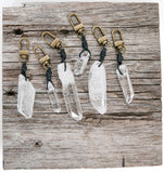 A collection of clear quartz crystal keychains with metal rings, displayed on a wooden surface.